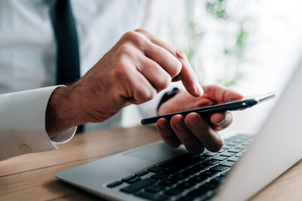 Mann mit Telefon in der Hand und Laptop am Tisch