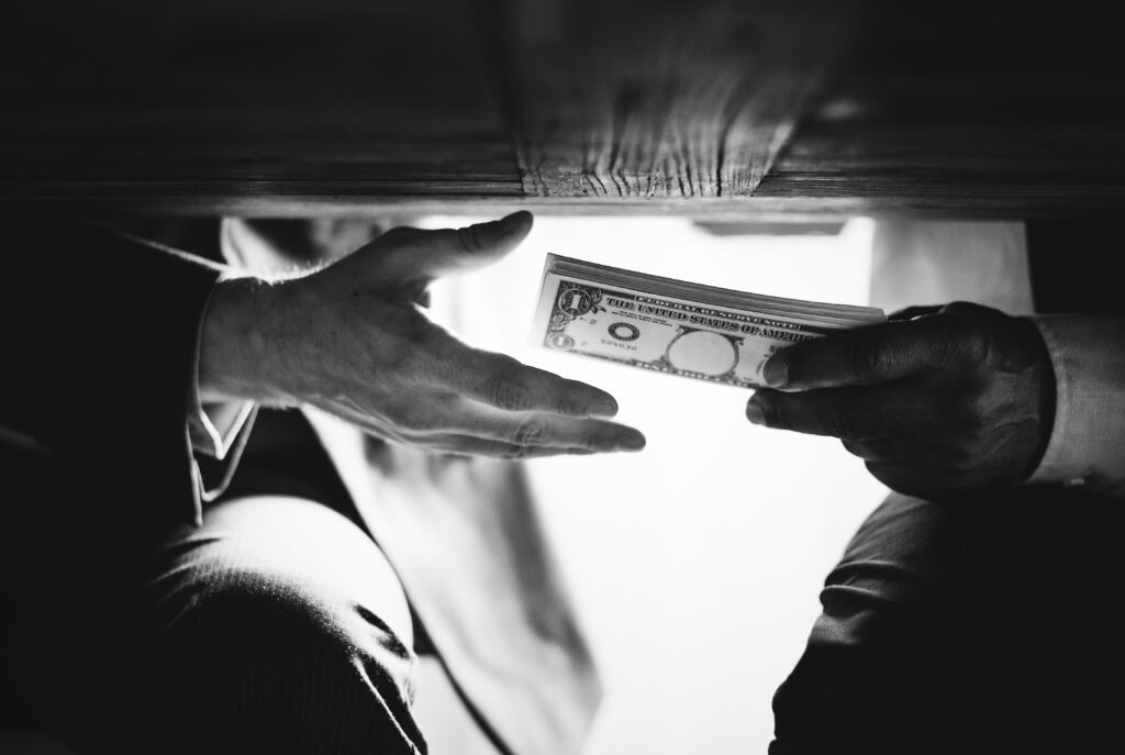 Hände reichen sich unter einem Tisch Geld