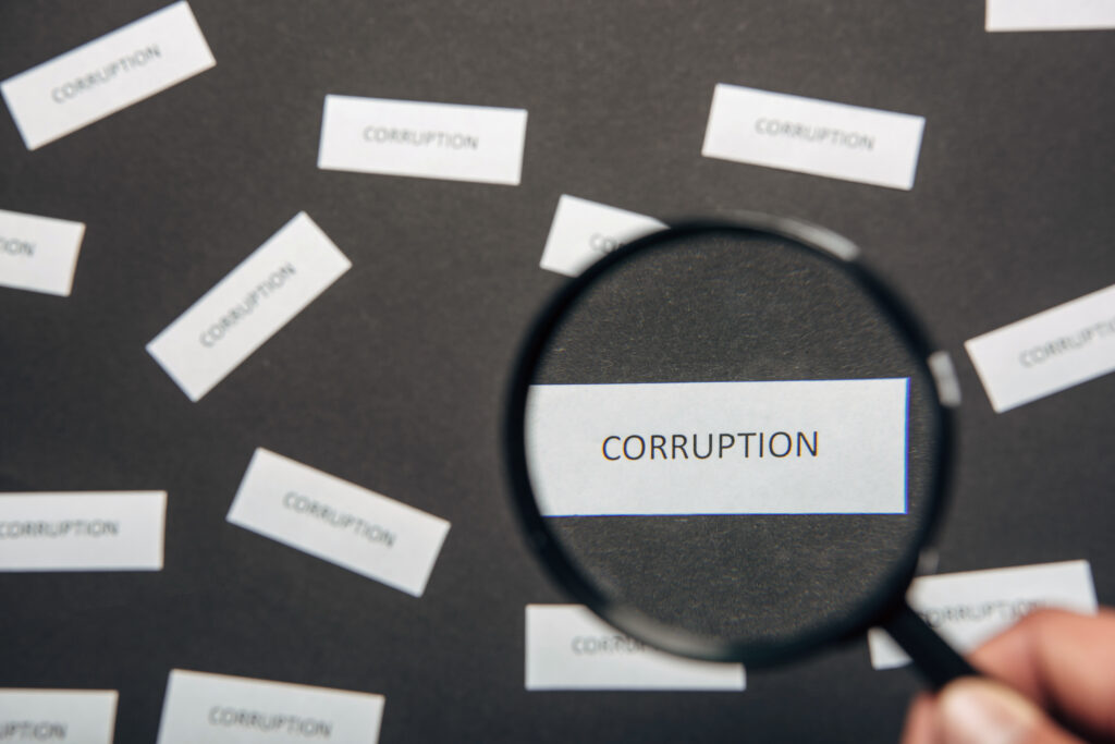 Hand hält Lupe und vergrößert das Wort "CORRUPTION"