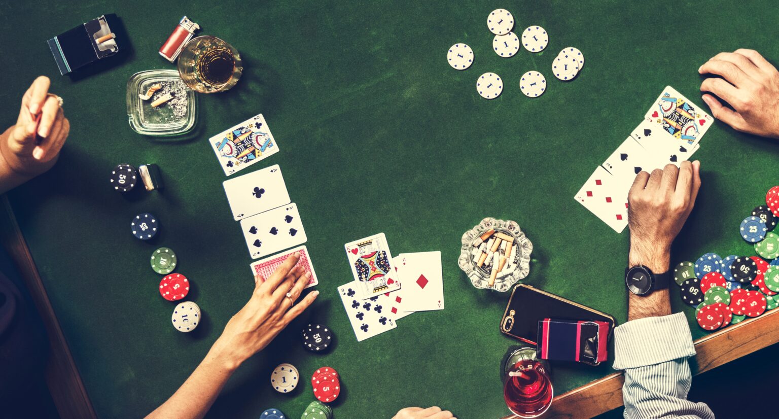 Ein grüner Tisch auf dem Würfel, Karten und andere Materialien für das Glücksspiel liegen und vier Hände auf diesem Tisch zu sehen sind