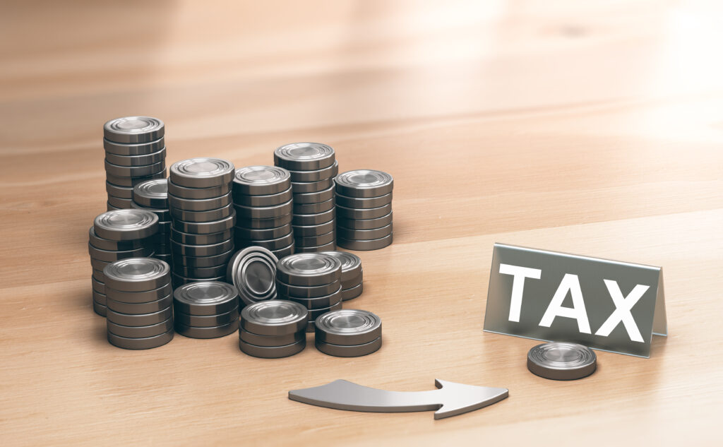 Aufgestapelte Münzen, ein Pfeil und ein Schild auf dem TAX geschrieben steht