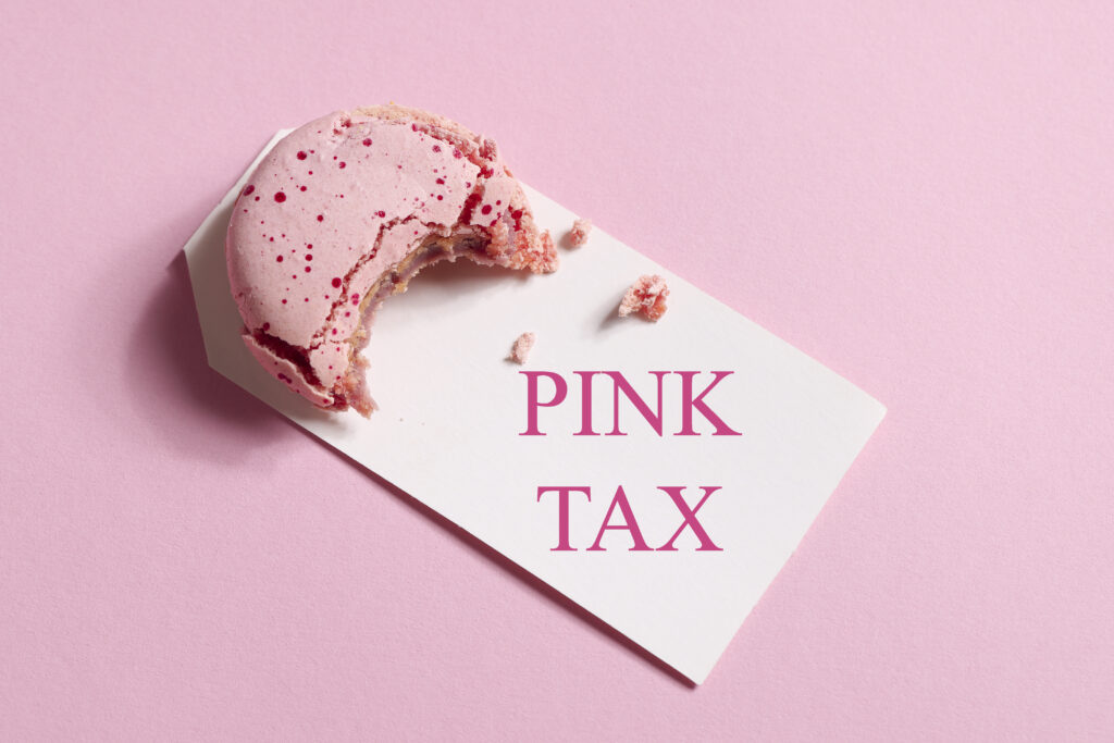 Rosaroter Hintergrund davo ein kleiner Keks mit pinker Glasur auf einem weißen Schild mit den Worten Pink Tax