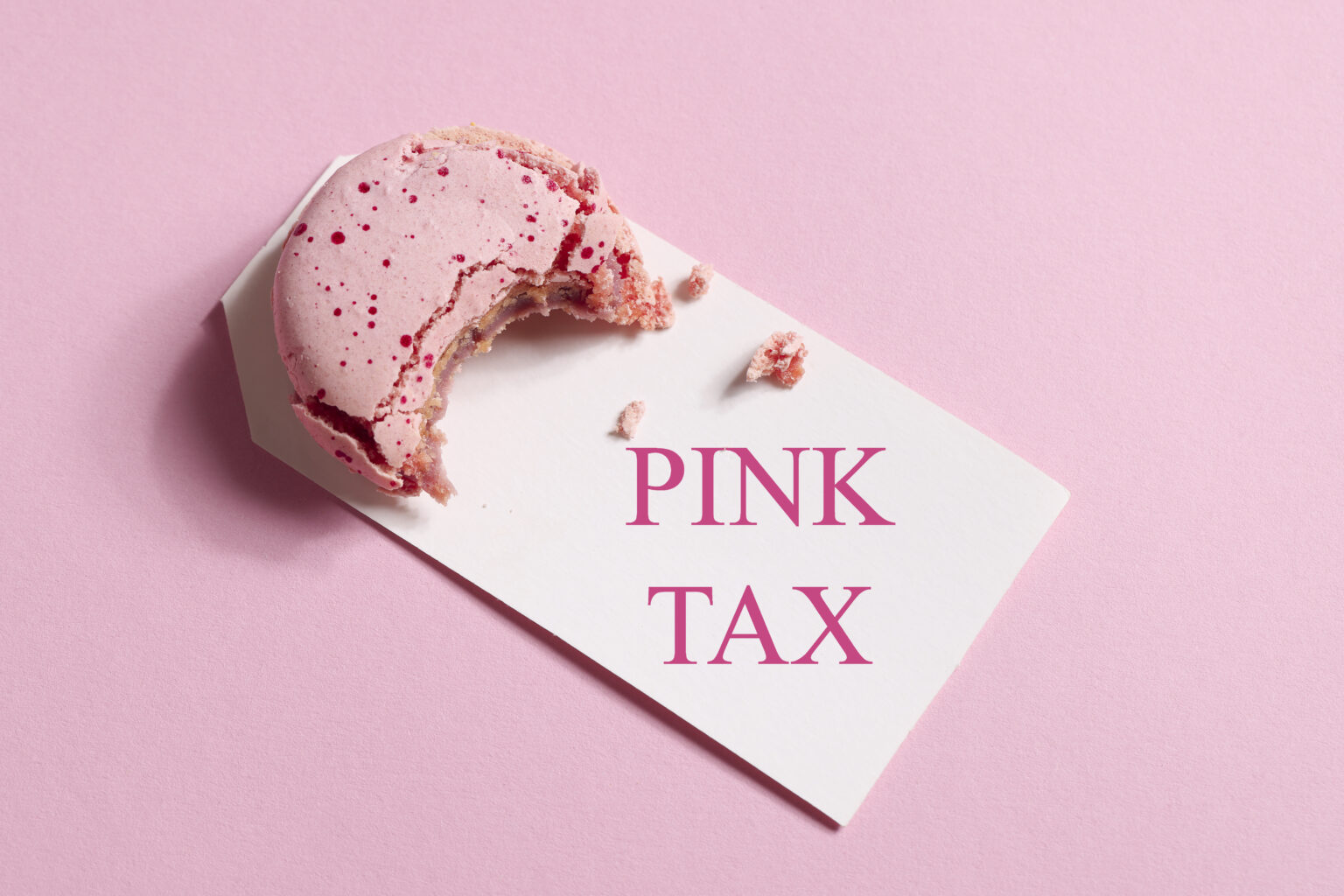 Rosaroter Hintergrund davo ein kleiner Keks mit pinker Glasur auf einem weißen Schild mit den Worten Pink Tax