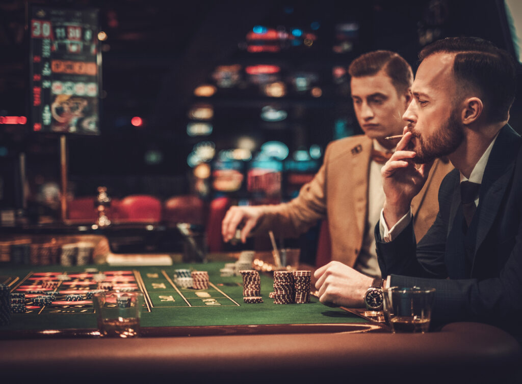 Zwei Männer sitzen an einem Tisch an dem Roulette gespielt wird und setzten ihre Steine