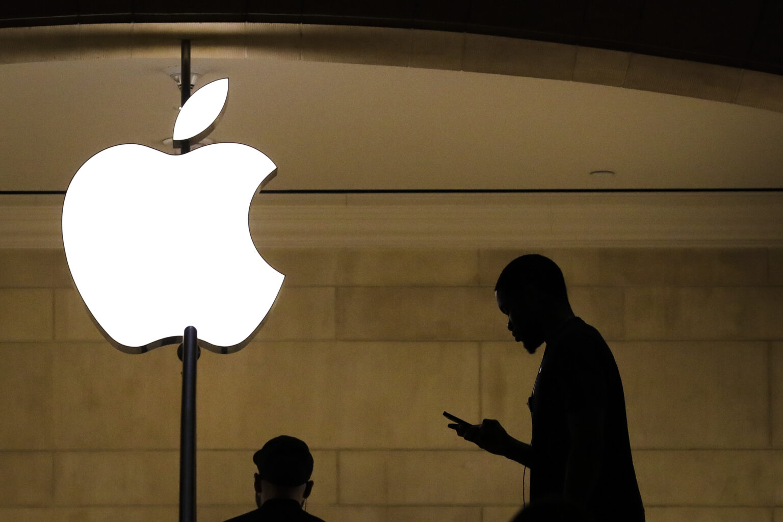 weißes Apple Logo vor einem braunen Hintergrund das zwei Menschen in schwarz zeigt