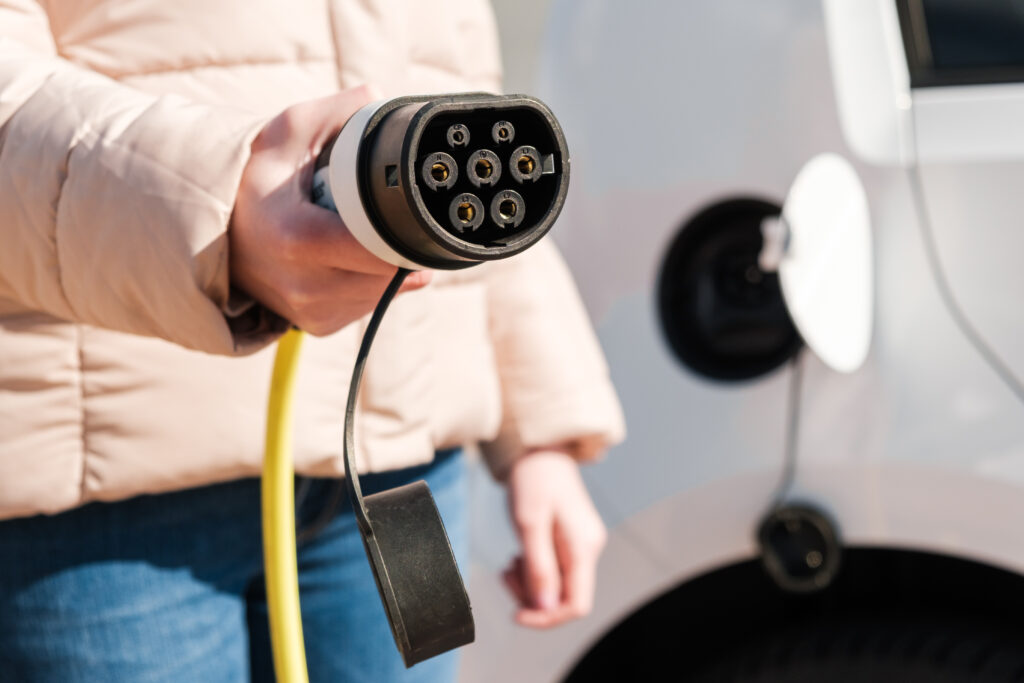 Mensch mit heller Jacke hält ein Ladegerät für E-Autos in die Kamera