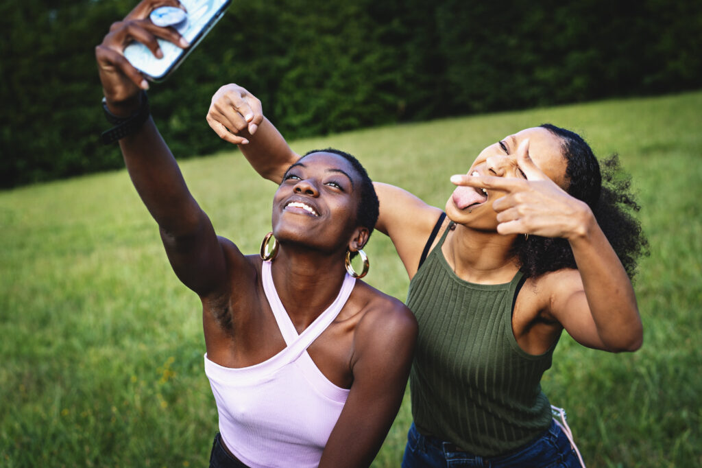 Zwei Frauen halten eine Handy in die Höhe und machen auf einer Wiese in Fitnesskleidung ein Selfie
