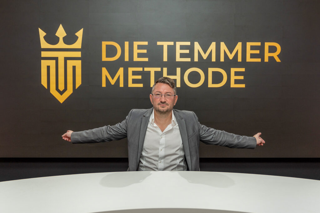 Walter Temmer sitzt vor großer Wand mit der Aufschrift "Die Temmer Methode"