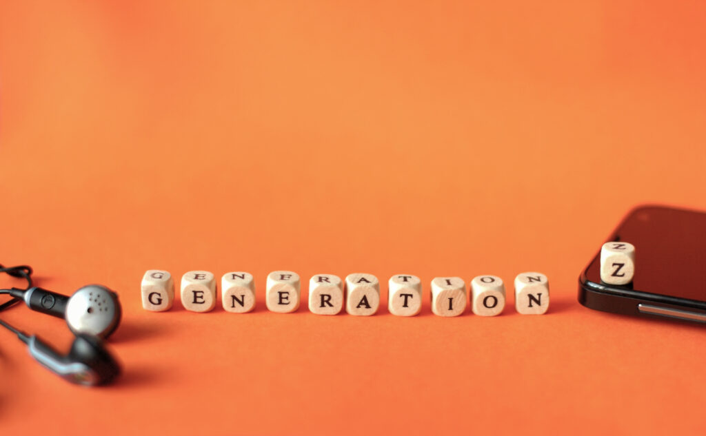 Generation Z in Blockbuchstaben auf Würfeln. Daneben liegen Kopfhörer und ein Smartphone auf orangem Hintergrund.
