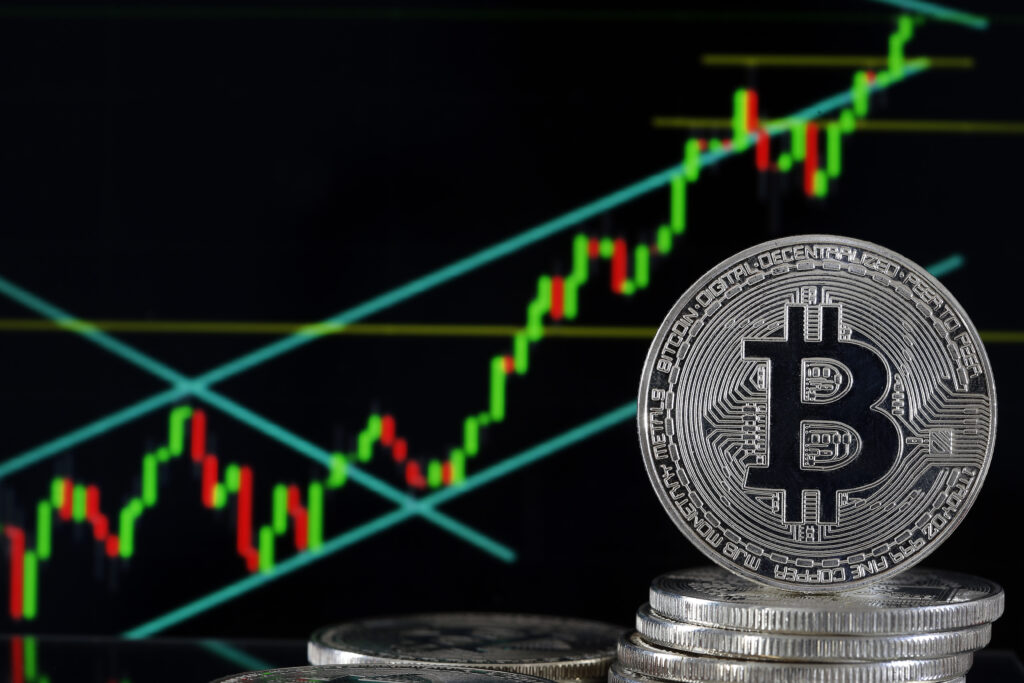 Aktienkurse die tendenziell steigen in grün, gelb und rot. Davor eine große Bitcoin-Münze