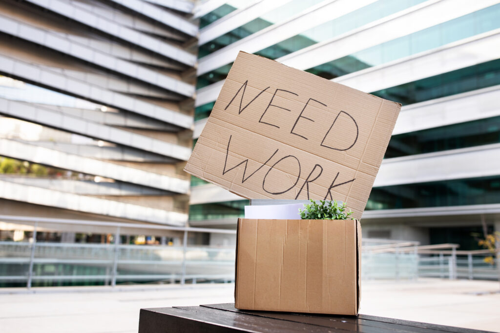 Schild aus Karton mit der Aufschrift: Need Work in einem Bürogebäude