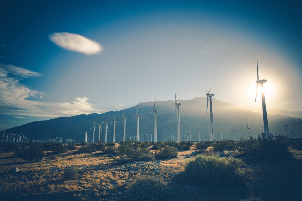 erneuerbare Energien Viele Windturbine stehen auf einem Feld. Dahinter ein Sonnenuntergang und der Blick auf einen Berg