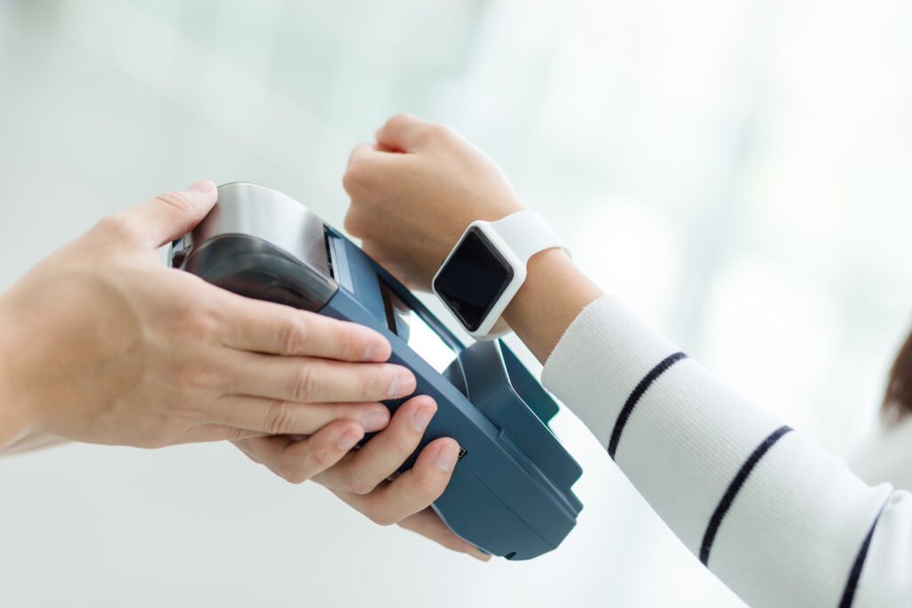 Frau mit einer Smart-Watch legt ihre Uhr auf ein Bankomatgerät das von einer anderen Hand gehalten wird
