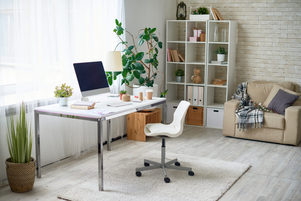 Büro mit Tisch und weißem Sessel. Darunter ein heller Teppich und Ein Regal rechts vom Tisch