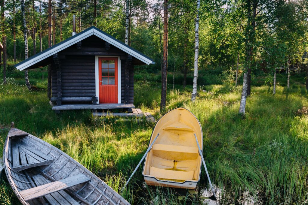 Finnland Kleines Saunahaus das im Wald steht. Davor ein gelbes kleines Boot