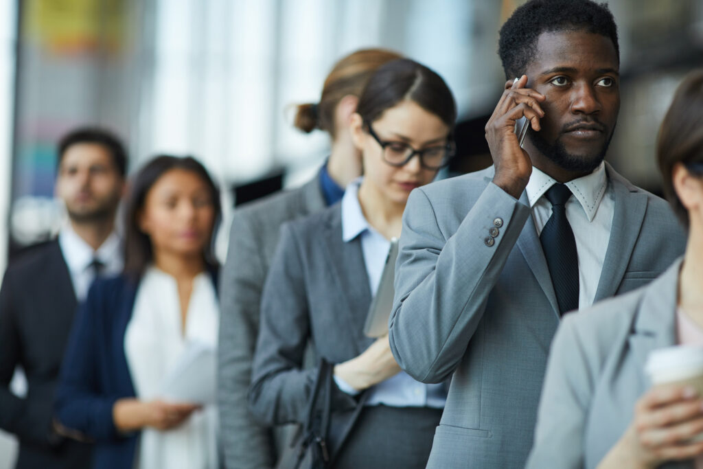 Menschen, die sich in einer Schlange anstellen und dabei auf ihre Handys blicken oder telefonieren