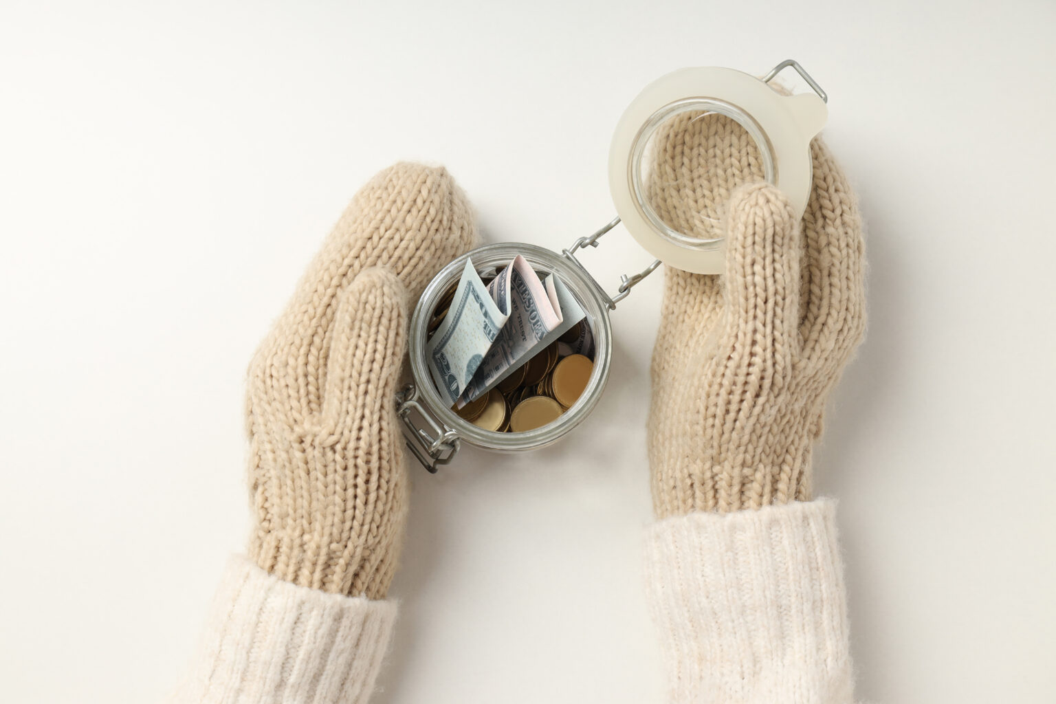 Hände mit weiße gestrickten Handschuhen die ein Glas halten indem ein paar Geldscheine und Münzen sind