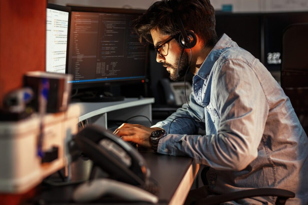 Programmierer sitzt vor mehreren PCs und trägt dabei ein Headset