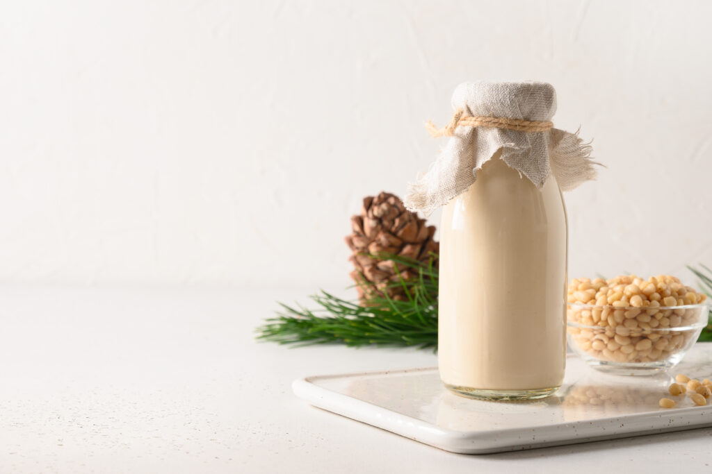 Milchflasche daneben Zedernnüsse und eine Zeder auf einem weißen Tisch