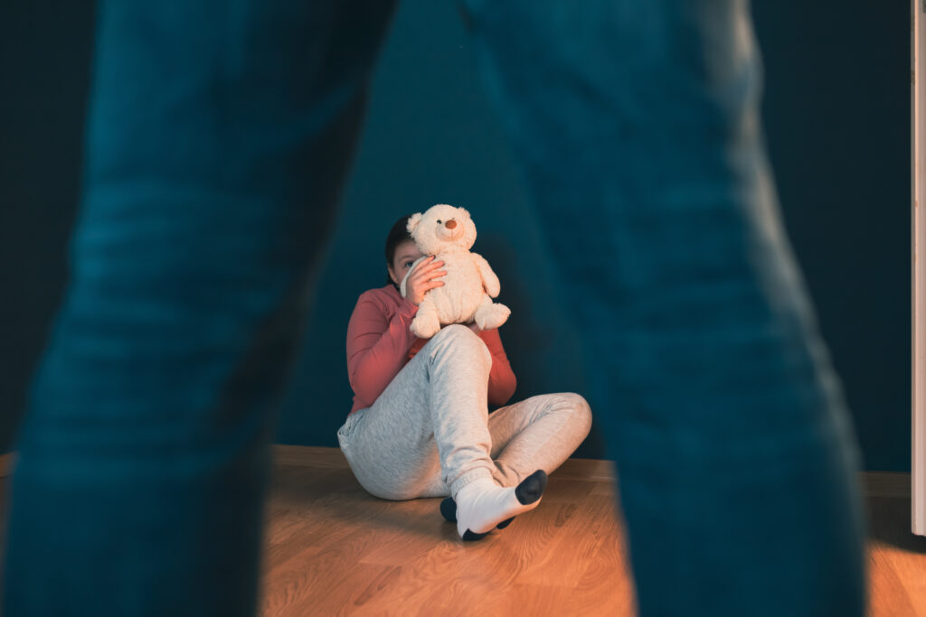 Kind hält Teddy-Bär und sitzt ängstlich am Boden