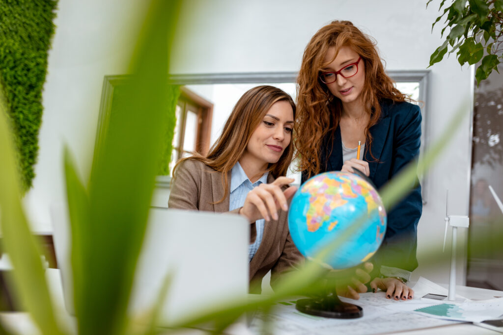 Zwei Frauen deuten auf einen Globus der auf einem Tisch steht