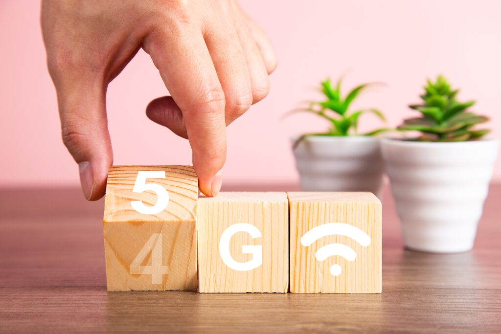 5 G auf Klötzen geschrieben. Dahinter zwei Pflanzen in kleinen Töpfen und eine Hand die einen Würfel von 4 auf 5 umdreht