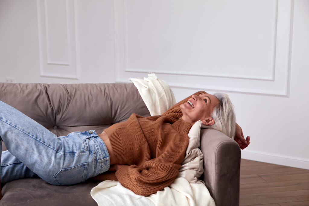 Frau mit weißen Haaren liegt am Sofa und lacht
