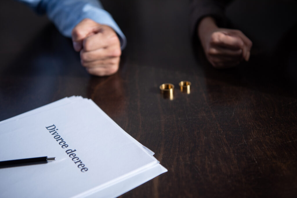 Tisch mit Scheidungsdokumenten zwei Eheringen und zwei Händen die zur Faust geballt sind